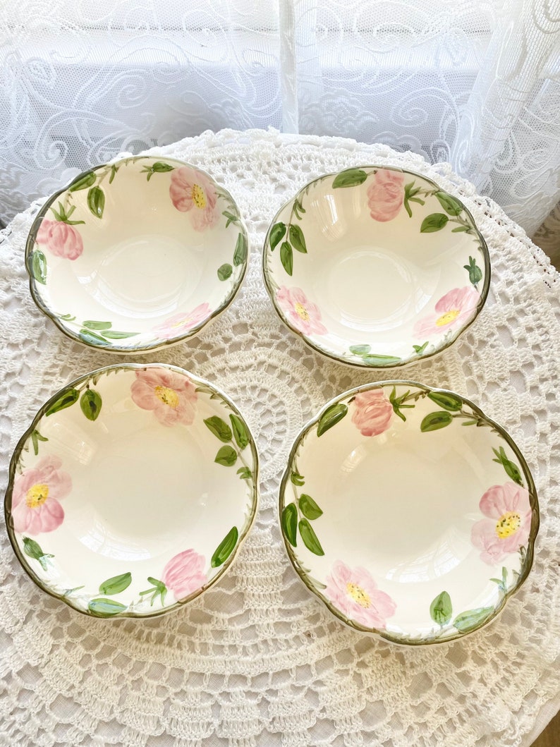 May include: Set of four white ceramic bowls with a floral design featuring pink roses and green leaves. The bowls have a scalloped edge and are perfect for serving soup, salad, or dessert.