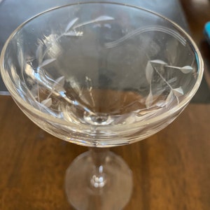 May include: A clear glass stemmed cocktail glass with a delicate etched floral design.
