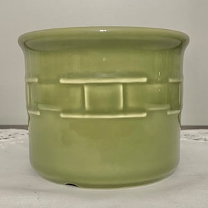 May include: A green ceramic planter with a basket weave design. The planter is glazed and has a smooth finish.