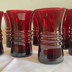 Pode incluir: Conjunto de seis copos de vidro vermelho-rubi com design canelado. Os copos são transparentes e têm um aspeto vintage.