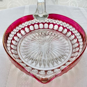 Könnte beinhalten: Eine klare Glasschale mit rosafarbenem Rand und einem klaren Glasgriff. Die Schale hat ein dekoratives Muster aus Kreisen und Linien.