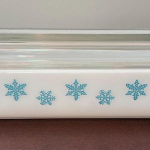 May include: A rectangular white casserole dish with a clear glass lid. The dish is decorated with a pattern of blue snowflakes. The dish is designed for baking and serving.