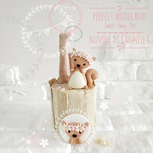 May include: A woodland-themed cake decorated with a brown and white squirrel figurine wearing a pink flower crown. The cake is shaped like a tree stump and has a brown and white squirrel figurine with a pink flower crown on top. The cake is decorated with a white background and pink flowers.
