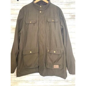 May include: A dark green, quilted, zip-up jacket with a stand-up collar and multiple pockets. The jacket has a brown leather patch with the text "Billy Joe" on the bottom right side.