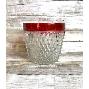 May include: A clear glass drinking glass with a diamond pattern and a red rim.