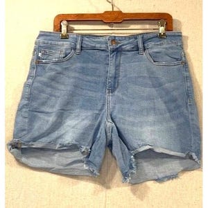 May include: Light blue denim shorts with a frayed hem, featuring classic five-pocket styling and a button closure. The shorts are hanging on a wooden hanger.