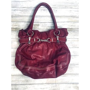 May include: A burgundy leather handbag with silver hardware and a white stitch detail. The bag has a top handle and a flap closure.