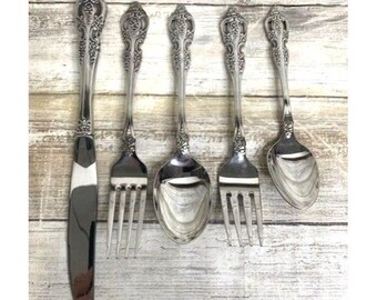 May include: Set of five silver-plated flatware pieces with ornate handles. The set includes a knife, two forks, and two spoons.