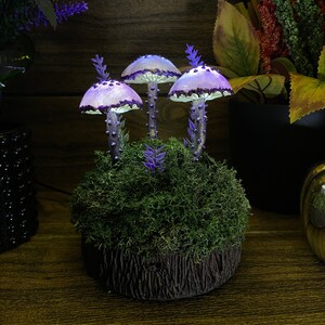 May include: Three purple and white mushroom shaped lamps with a mossy base. The lamps are lit and glow softly.