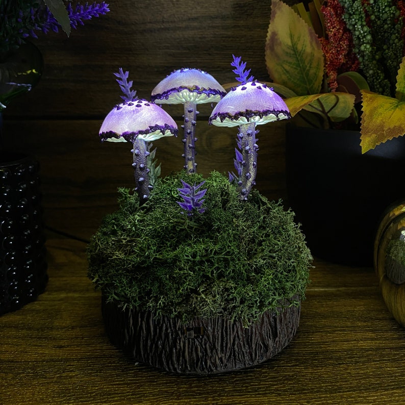 May include: Three purple and white mushroom shaped lamps with a mossy base. The lamps are lit and glow softly.