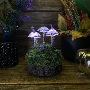 May include: A purple and white mushroom lamp with a mossy base. The lamp is lit and casts a warm glow.