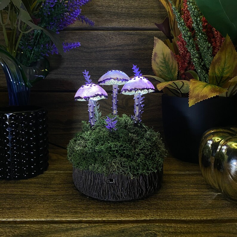 May include: A purple and white mushroom lamp with a mossy base. The lamp is lit and casts a warm glow.
