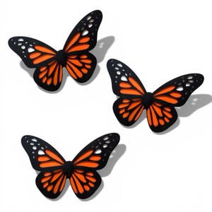 May include: Three decorative butterfly ornaments. Each butterfly features a black outline with orange and white wing details. The butterflies are arranged on a white background, with shadows suggesting they are slightly raised.