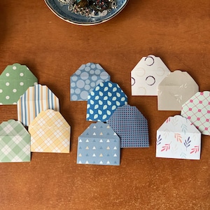 May include: Ten small, decorative envelopes with different patterns. The envelopes are made of paper and have a variety of colours, including green, blue, yellow, and pink. The envelopes are all different sizes and shapes.