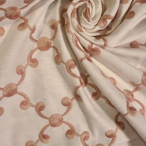 May include: White fabric with a delicate pattern of pink embroidered swirls and circles.
