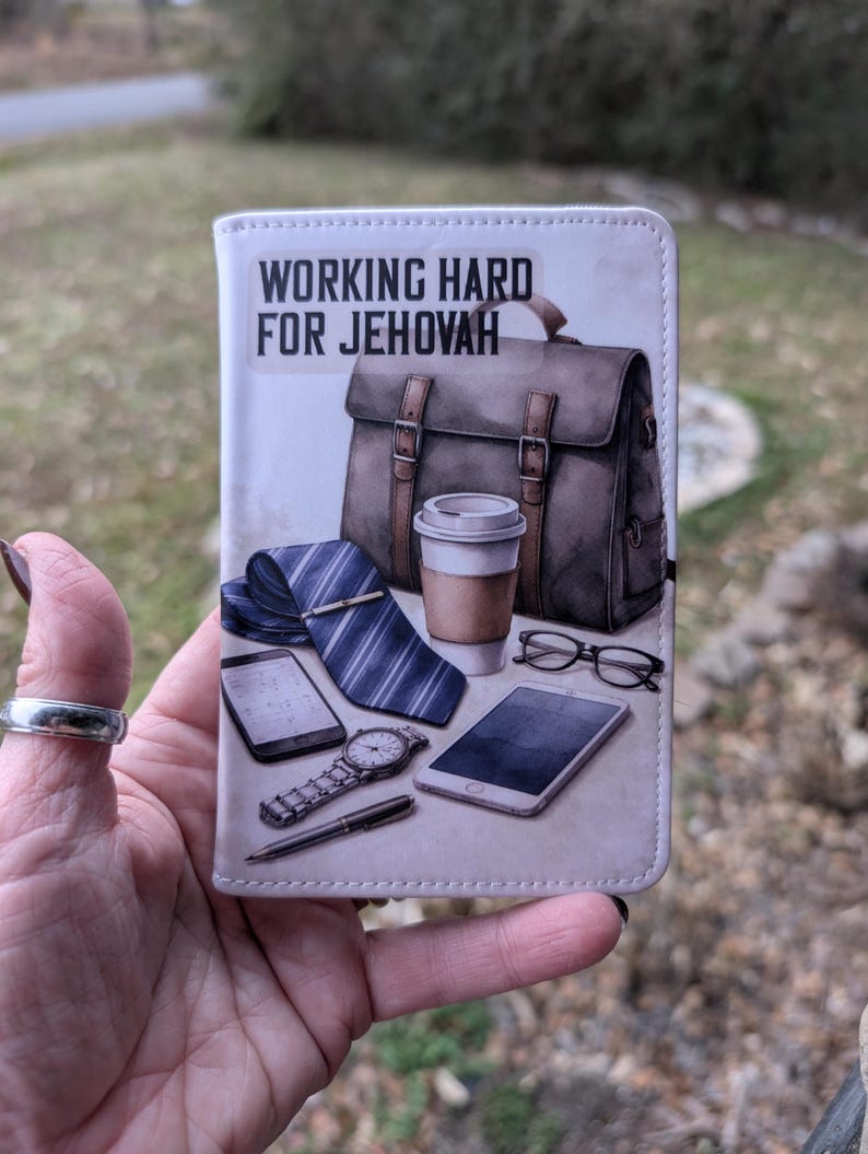 Puede incluir: Una cartera blanca con el texto "WORKING HARD FOR JEHOVAH" y una ilustraci&oacute;n de un malet&iacute;n, corbata, taza de caf&eacute;, reloj, gafas y tel&eacute;fonos inteligentes. La cartera se sostiene en una mano.