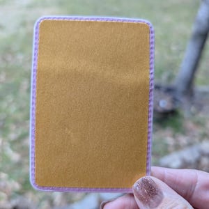 May include: A gold-colored sticker with a pink border. The sticker has a stitched edge.