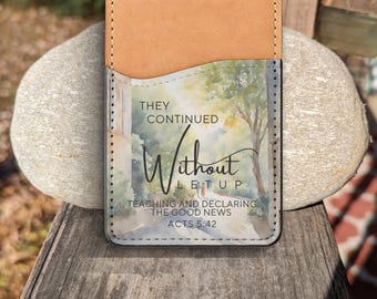 May include: A brown leather wallet with a pocket for cards and a watercolor design of a path through a forest. The text "They continued without letup teaching and declaring the good news Acts 5:42" is printed on the wallet.