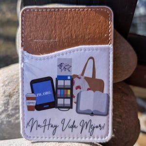 May include: A white phone case with a brown leather flap. The case features a design of a coffee cup, a tablet with the text "JW.ORG", a book, a tote bag, and a magazine. The text "No Hay Vida Mejor!" is printed on the case.