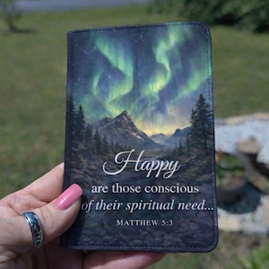 May include: A small, rectangular wallet featuring a landscape with the aurora borealis and mountains. The text "Happy are those conscious of their spiritual need..." and "MATTHEW 5:3" are displayed on the front.