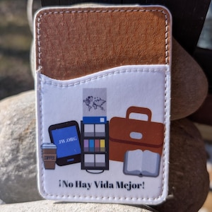 May include: A white leather card holder with a brown leather flap. The front of the card holder features a colorful illustration of a coffee cup, a phone, a briefcase, a book, and a magazine. The text "JW.ORG" and "&iexcl;No Hay Vida Mejor!" is printed on the card holder.