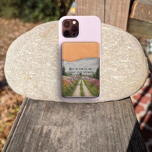 May include: A purple phone case with a brown leather wallet attached. The wallet has a scenic image and the text "BUT AS FOR US, WE CANNOT STOP SPEAKING ABOUT THE THINGS WE HAVE SEEN AND HEARD ACTS 4:20".