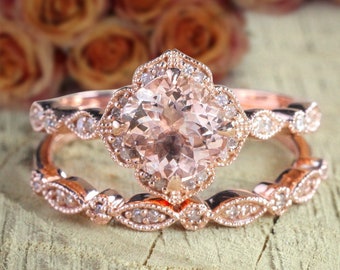 May include: A rose gold engagement ring set with a large, round, peach-colored gemstone surrounded by smaller diamonds. The band is adorned with delicate, floral-inspired details.