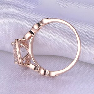 May include: A rose gold engagement ring with a square-shaped center stone surrounded by smaller stones. The ring has a delicate, intricate design.