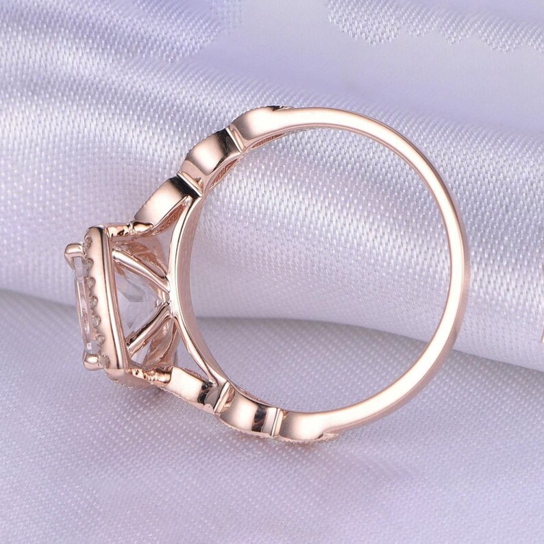 May include: A rose gold engagement ring with a square-shaped center stone surrounded by smaller stones. The ring has a delicate, intricate design.