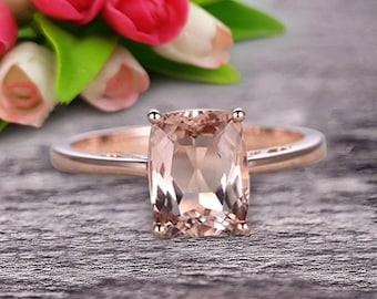 May include: A rose gold engagement ring with a cushion-cut morganite gemstone. The ring is set on a simple band.