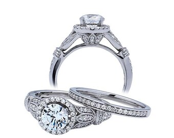 Puede incluir: Un conjunto de anillos de compromiso de plata con una piedra central redonda y un halo de piedras más pequeñas. La banda está decorada con detalles intrincados y presenta una banda de boda a juego.