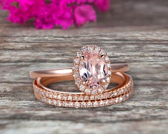 Op de afbeelding: Een verlovingsring van roségoud met een grote ovale morganiet-edelsteen omringd door een halo van kleinere diamanten. De ring wordt geleverd met twee bijpassende roségoud banden, elk bezet met een rij diamanten.