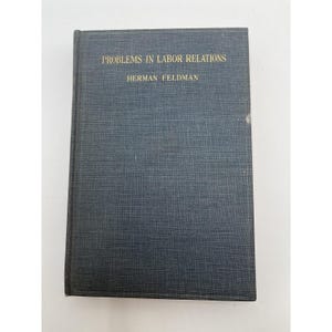 Può includere: Un libro con copertina rigida di colore blu scuro. Il titolo "PROBLEMS IN LABOR RELATIONS" e l'autore Herman Feldman sono in lettere dorate. Il libro è di forma rettangolare.