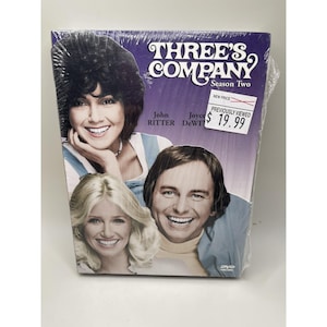 May include: A DVD of the television show "Three's Company," Season Two. The cover features images of the show's stars, with the show's title in a stylized font. The DVD is sealed in plastic.