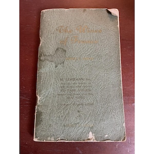 May include: Vintage green booklet titled "The Wines of France" with gold lettering. The cover shows wear and tear, with visible stains and a worn corner. The booklet includes the name "M. Lehmann, Inc." and an address in New York.