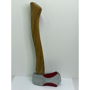 Puede incluir: Hacha con mango de madera y cabeza plateada con detalles rojos. El mango es curvo y de madera marrón claro. La cabeza del hacha tiene un acabado plateado con diseños curvos rojos.