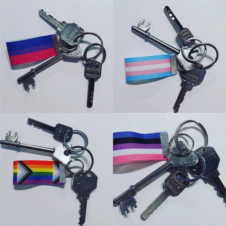 Puede incluir: Llaveros con cintas con los colores de las banderas del orgullo bisexual, transg&eacute;nero, no binario y progresista. Cada llavero contiene varias llaves en un anillo de metal plateado.