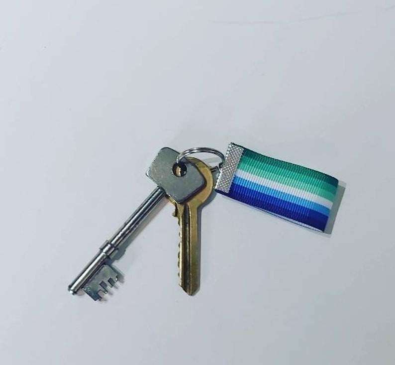 May include: Two keys on a silver key ring with a blue, white, and green ribbon attached. The ribbon has a white border.