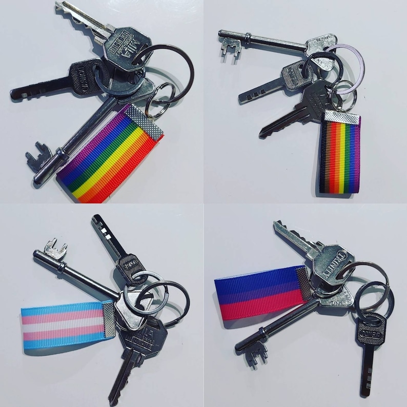 Puede incluir: Un conjunto de llaves en llaveros plateados, cada uno con una cinta de colores. Las cintas muestran las banderas del arco&iacute;ris, transg&eacute;nero y bisexual. Las llaves son de varios tama&ntilde;os y formas.