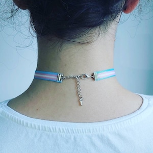 May include: A light blue, pink, and white ribbon choker necklace with a silver clasp.