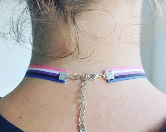 Op de afbeelding: Een chokerketting met een roze, wit, blauw en zwart lint, met een zilveren ketting en sluiting.