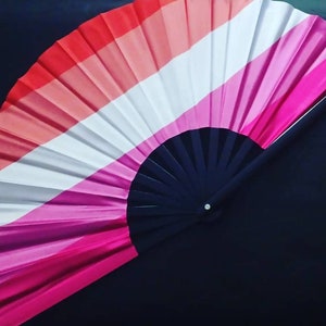 May include: A hand fan with a black handle and a pink, white, and red striped fabric design.