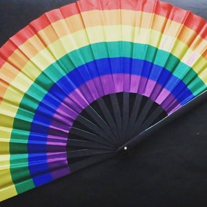May include: A rainbow-colored folding fan with a black handle. The fan is made of fabric and has a rainbow pattern.