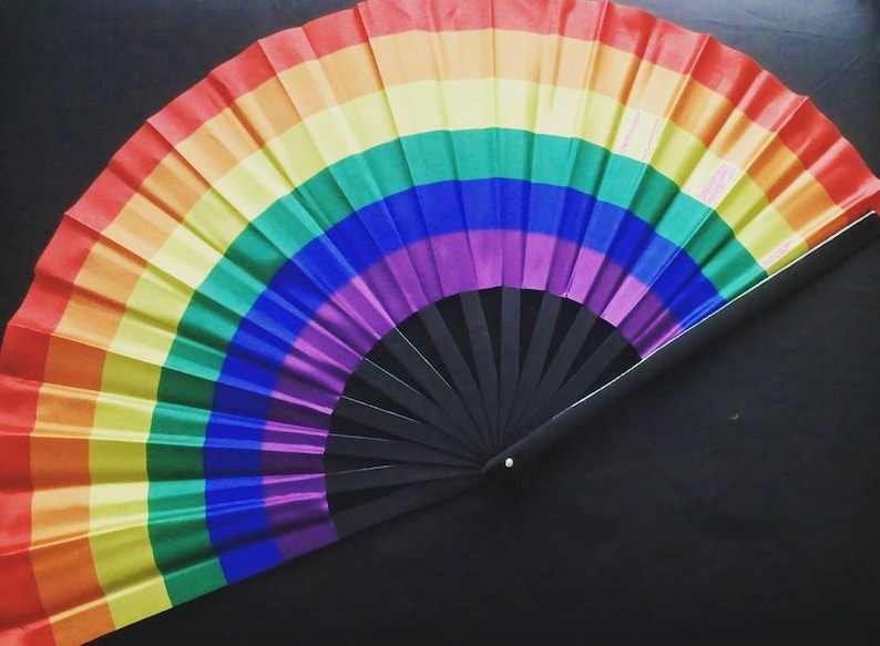 May include: A rainbow-colored folding fan with a black handle. The fan is made of fabric and has a rainbow pattern.