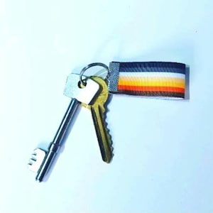 May include: A set of keys with a silver key and two gold keys attached to a black, white, orange, and yellow striped key chain.