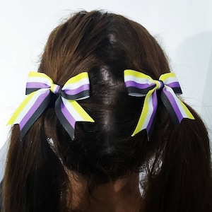 May include: Two yellow, purple, and black ribbon bows tied in pigtails. The bows are made of striped ribbon and are tied in a simple bow shape.