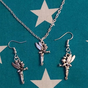 Puede incluir: Un conjunto de collar y pendientes de plata con un dije de hada. El hada está representada con las alas extendidas y sosteniendo una varita mágica. El collar tiene una delicada cadena de plata.