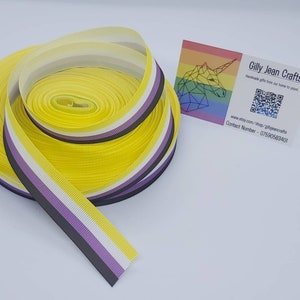 May include: A roll of yellow, white, purple and black striped ribbon. The ribbon is a representation of the non-binary pride flag.