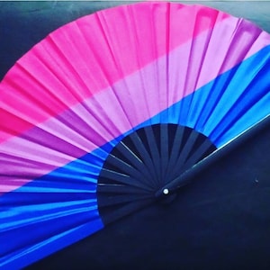 May include: A black folding fan with a pink, purple, and blue silk fabric design. The fabric is folded in a fan shape and has a black handle.
