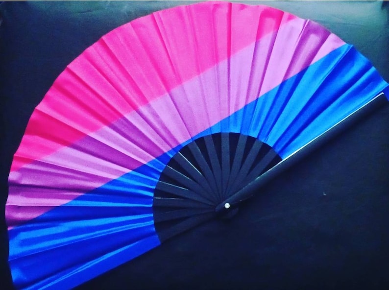 May include: A black folding fan with a pink, purple, and blue silk fabric design. The fabric is folded in a fan shape and has a black handle.